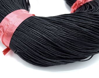 May include: A close-up of a spool of black waxed cotton cord. The cord is tightly wound and has a smooth, polished finish.