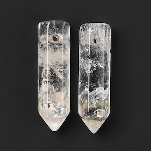 Può includere: Due punte di cristallo di quarzo trasparente con un foro praticato nella parte superiore. I cristalli misurano circa 7,5 cm di lunghezza e hanno una punta appuntita.