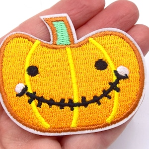 Peut inclure: Écusson brodé représentant une citrouille souriante. La citrouille est orange avec une tige verte et un bord blanc. Le visage a des yeux noirs et une bouche cousue et dentelée. Un article décoratif amusant pour Halloween.