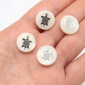 Peut inclure: Quatre boutons ronds blancs avec un motif de tortue. Deux tortues sont noires et deux tortues sont argentées.