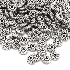 Könnte beinhalten: Ein großer Haufen silberner Metallperlen mit einem dekorativen, gedrehten Design. Die Perlen haben ein Loch in der Mitte zum Auf fädeln.