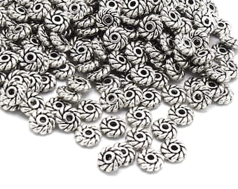 May include: A large pile of silver metal beads with a decorative, twisted design. The beads have a hole in the center for stringing.