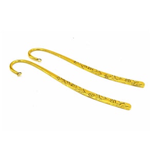 Könnte beinhalten: Zwei goldene Lesezeichen aus Metall mit einem floralen Design. Die Lesezeichen sind oben gebogen, um eine Seite zu halten.