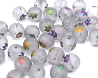 May include: A collection of frosted glass beads, each adorned with a colorful maple leaf design. The beads are round and have a subtle, swirling texture. The maple leaf designs feature a gradient of colors, including green, gold, and purple.