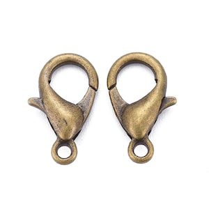 Pode incluir: Dois fechos de lagosta de metal dourado antigo com um anel redondo na parte inferior.