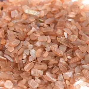 Peut inclure: Gros plan sur un tas de petites pierres de soleil irrégulières, de couleur rose clair et blanche. Les pierres sont translucides et ont une qualité chatoyante et irisée.