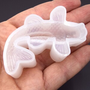 K&ouml;nnte beinhalten: Eine transparente Silikonform in Form eines Koi-Karpfens. Die Form ist zum Erstellen von Kunsthandwerk aus Harz gedacht.