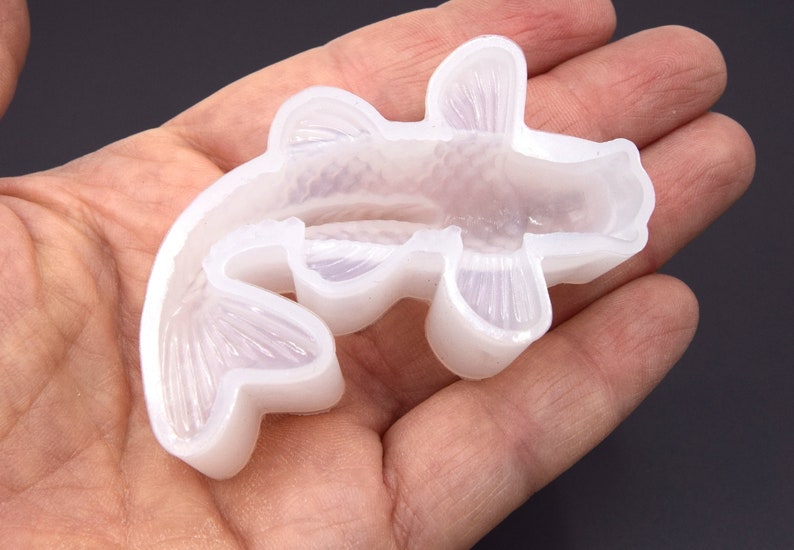 K&ouml;nnte beinhalten: Eine transparente Silikonform in Form eines Koi-Karpfens. Die Form ist zum Erstellen von Kunsthandwerk aus Harz gedacht.
