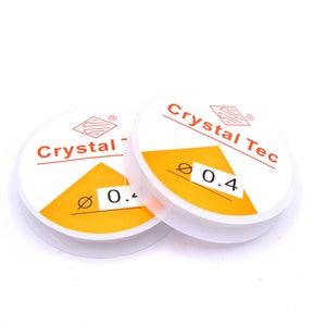May include: Two spools of white elastic cord with orange labels. The labels read "Crystal Tec" and "Ø 0.4".