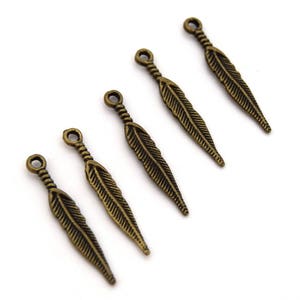 Puede incluir: Cinco abalorios de plumas de bronce antiguo con un bucle en la parte superior para sujetar a joyas o manualidades.