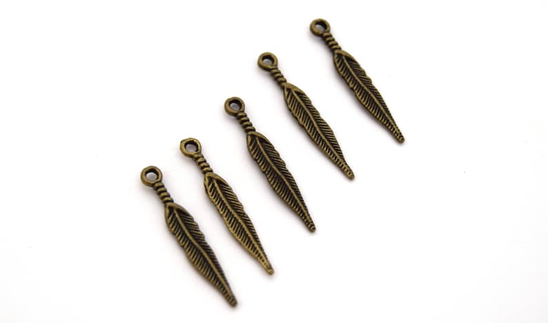 Puede incluir: Cinco abalorios de plumas de bronce antiguo con un bucle en la parte superior para sujetar a joyas o manualidades.