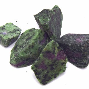 Puede incluir: Cinco piedras ásperas, verdes y moradas con motas negras. Las piedras tienen una forma irregular y un acabado natural sin pulir.