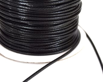 May include: A spool of black waxed cotton cord. The cord is wound tightly around a white cardboard spool.