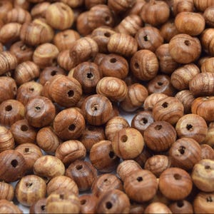 Può includere: Primo piano di numerose perline di legno rotonde, in varie tonalità di marrone. Ogni perlina ha un foro centrale e mostra venature del legno visibili. Ideali per la creazione di gioielli o lavori artigianali. Le perline sono probabilmente misurate in centimetri.