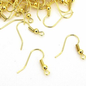 May include: A close-up of gold-toned earring hooks with a spring-loaded closure. The hooks are made of metal and have a smooth, polished finish.