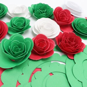 May include: An assortment of paper flowers in red, green, and white. The flowers are in various stages of assembly, with some fully formed and others as individual petals and leaves. The arrangement is on a white background.