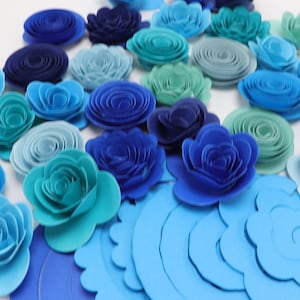 May include: Assortment of blue, teal, and aqua paper flowers. The flowers are layered and have a 3D effect. They are perfect for adding a touch of elegance to any occasion.