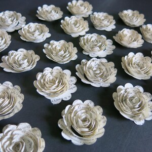 Peut inclure: Une collection de 18 fleurs en papier blanc cass&eacute; avec un bord festonn&eacute;. Les fleurs sont faites &agrave; partir de pages d'un livre et ont un aspect vintage.