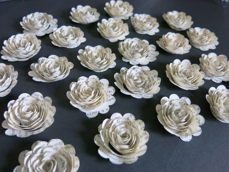 Peut inclure: Une collection de 18 fleurs en papier blanc cass&eacute; avec un bord festonn&eacute;. Les fleurs sont faites &agrave; partir de pages d'un livre et ont un aspect vintage.