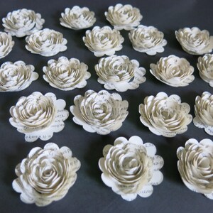 Peut inclure: Une collection de 20 fleurs en papier de couleur cr&egrave;me, chacune avec un design unique et superpos&eacute;. Les fleurs sont faites de pages de livres recycl&eacute;es et ont un aspect vintage.