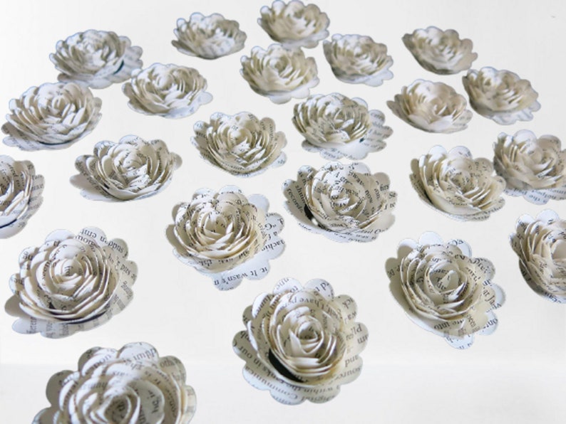 Peut inclure: Une collection de 20 fleurs en papier blanc, chacune faite &agrave; partir de pages d'un livre. Les fleurs sont dispos&eacute;es en rang&eacute;es sur une surface blanche.