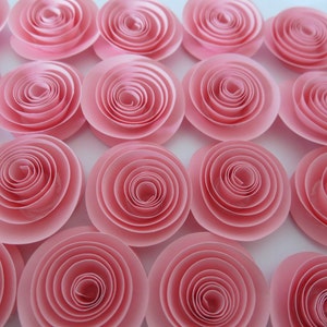 May include: A collection of 15 pink paper rosettes, each with a layered, spiral design. The rosettes are arranged in a grid pattern on a white background.