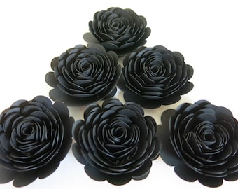 Peut inclure: Six roses en papier noir disposées en forme de triangle. Les roses sont composées de plusieurs couches de papier, ce qui leur donne un aspect plein et réaliste.