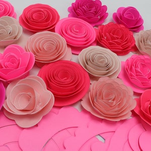 May include: A collection of pink, red, and white paper flowers. The flowers are layered and have a ruffled appearance. There are also several pink paper circles in the background.