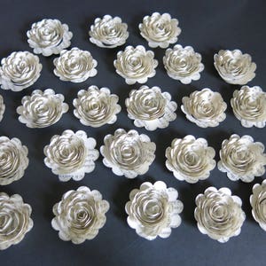 Peut inclure: Une collection de 20 fleurs en papier blanc avec un design de page de livre vintage. Les fleurs sont dispos&eacute;es en cercle sur une surface grise.
