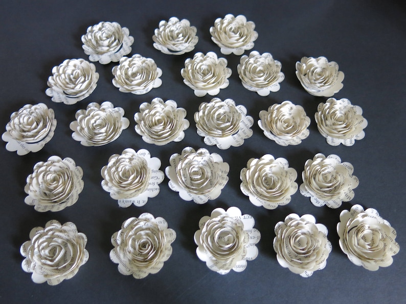 Peut inclure: Une collection de 20 fleurs en papier blanc avec un design de page de livre vintage. Les fleurs sont dispos&eacute;es en cercle sur une surface grise.
