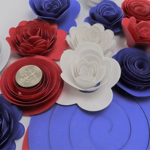 May include: A collection of paper flowers in red, white, and blue. The flowers are layered and have a spiral design. There are also some flat, circular pieces of paper in blue.