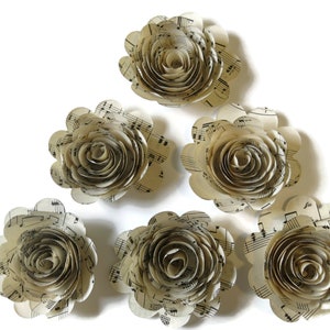 May include: Six paper flowers made from sheet music. The flowers are cream colored and have a spiral design.