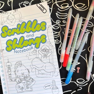 May include: A notebook with the text "Scribbles and Shlongs" and illustrations, along with several gel pens with colorful ink. The notebook is open on a black and white patterned surface.