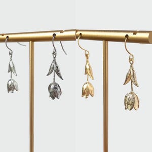 May include: Two pairs of flower-shaped earrings on a gold stand. One pair is silver and the other is gold.