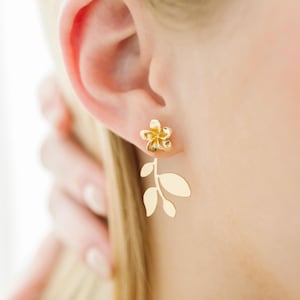 May include: Gold flower and leaf earrings. The flower is a simple design with five petals. The leaves are delicate and dangle below the flower.
