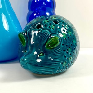 Peut inclure: Une figurine de hérisson en céramique bleu turquoise avec des yeux verts et des feuilles. La figurine a une surface texturée et est un objet décoratif.