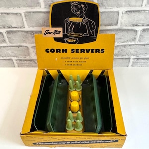 May include: A vintage Sow-Rite corn server set in a yellow cardboard display box. The set includes four dark green rectangular corn husk dishes and eight light green corn skewers, along with two yellow corn-shaped salt and pepper shakers.