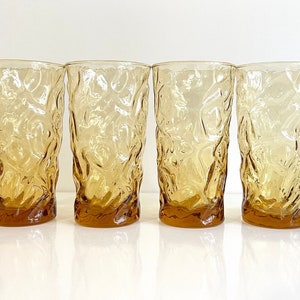 Op de afbeelding: Set van vier amberkleurige glazen met een getextureerd, geribbeld ontwerp. De glazen zijn helder en hebben een licht amberkleurige tint.