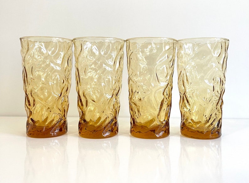 Op de afbeelding: Set van vier amberkleurige glazen met een getextureerd, geribbeld ontwerp. De glazen zijn helder en hebben een licht amberkleurige tint.