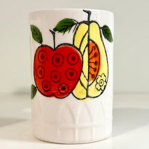Peut inclure: Une tasse en céramique blanche avec un motif stylisé d'une pomme rouge et d'une poire jaune avec des accents orange et vert.