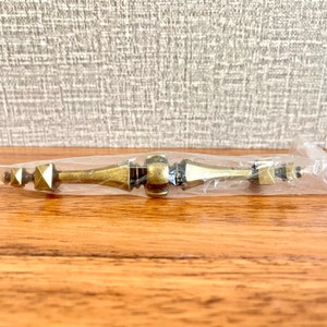 May include: A gold-toned cabinet pull with a geometric design. The pull is packaged in a clear plastic bag.