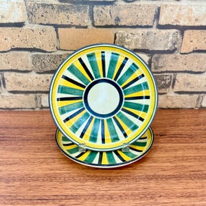 May include: Two ceramic plates with a yellow, green, and black striped design. The plates are stacked on top of each other.