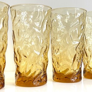 Op de afbeelding: Set van vier amberkleurige glazen met een getextureerd, geribbeld oppervlak. De glazen zijn helder en hebben een licht amberkleurige tint.
