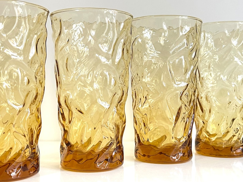 Op de afbeelding: Set van vier amberkleurige glazen met een getextureerd, geribbeld oppervlak. De glazen zijn helder en hebben een licht amberkleurige tint.