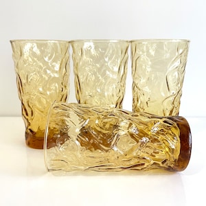 Op de afbeelding: Set van vier amberkleurige glazen met een getextureerd, geribbeld ontwerp. De glazen zijn helder en hebben een licht amberkleurige tint.