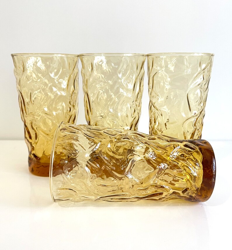 Op de afbeelding: Set van vier amberkleurige glazen met een getextureerd, geribbeld ontwerp. De glazen zijn helder en hebben een licht amberkleurige tint.