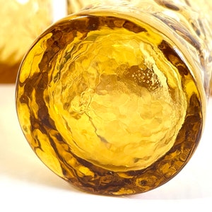 Op de afbeelding: Close-up van de bodem van een heldere amberkleurige glazen tumbler met een getextureerd oppervlak. Het glas heeft een dikke, afgeronde basis.