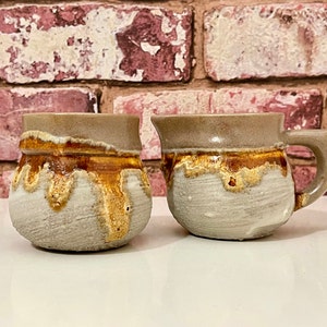 May include: A set of two ceramic mugs with a brown and white glaze. The mugs have a rustic, handmade look.