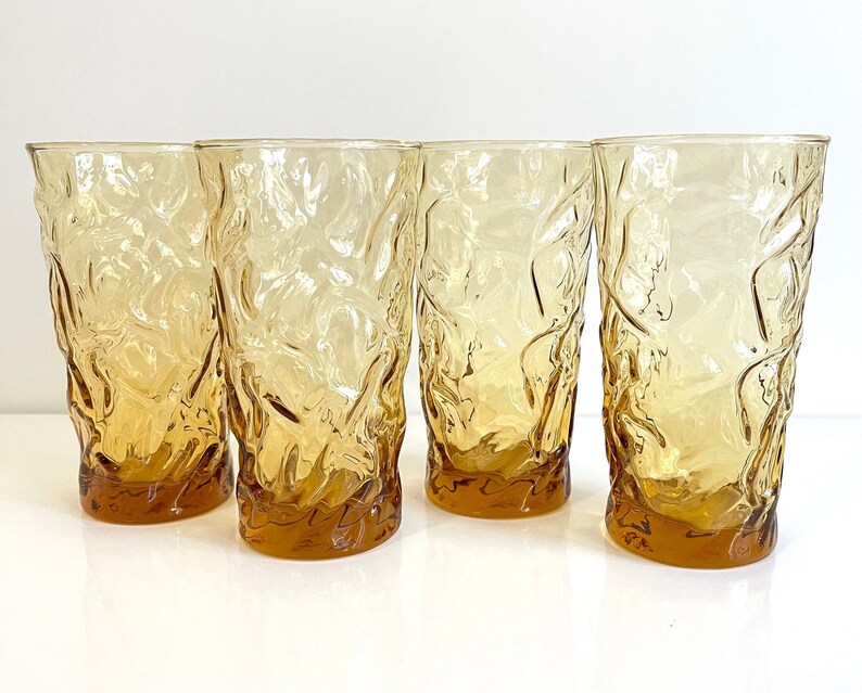 Op de afbeelding: Set van vier amberkleurige glazen met een getextureerd, golvend ontwerp. De glazen zijn helder en hebben een licht amberkleurige tint.