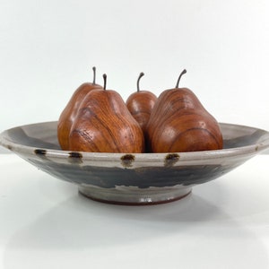 May include: A ceramic bowl with a black and white glaze, featuring a dark brown rim and four wooden pears inside.